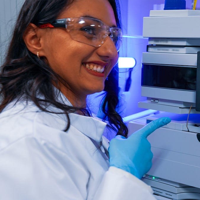 A smiling laboratory technician points to a machine.